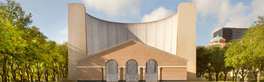 A brick building with curved walls and arches, surrounded by trees.